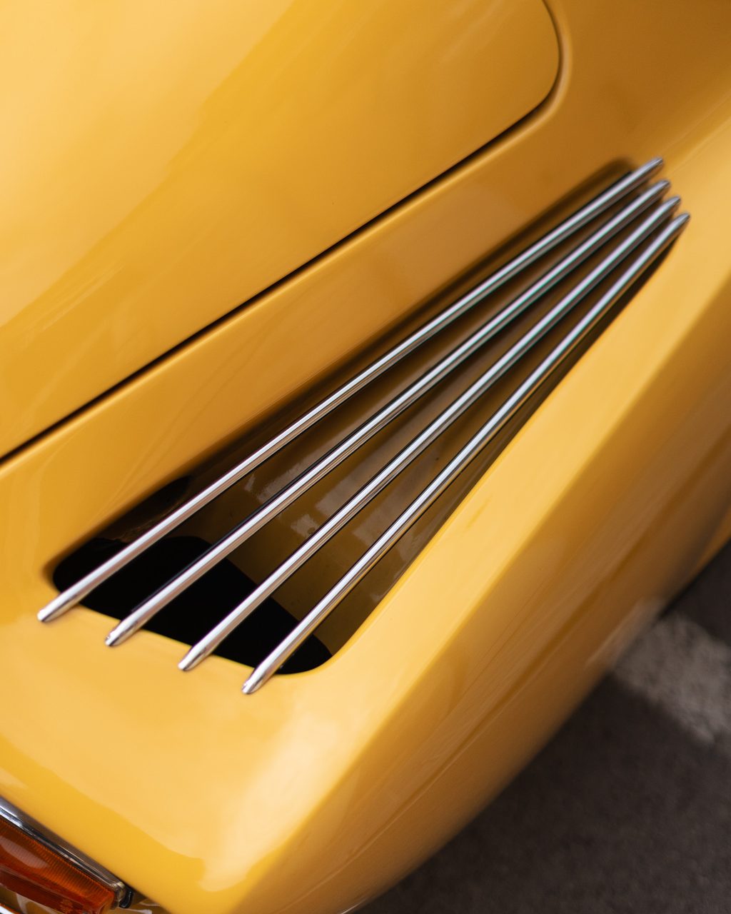 Detalle de las lamas metálicas de ventilación y la carrocería amarilla curvada de un Alpine A110 clásico en Madrid.
