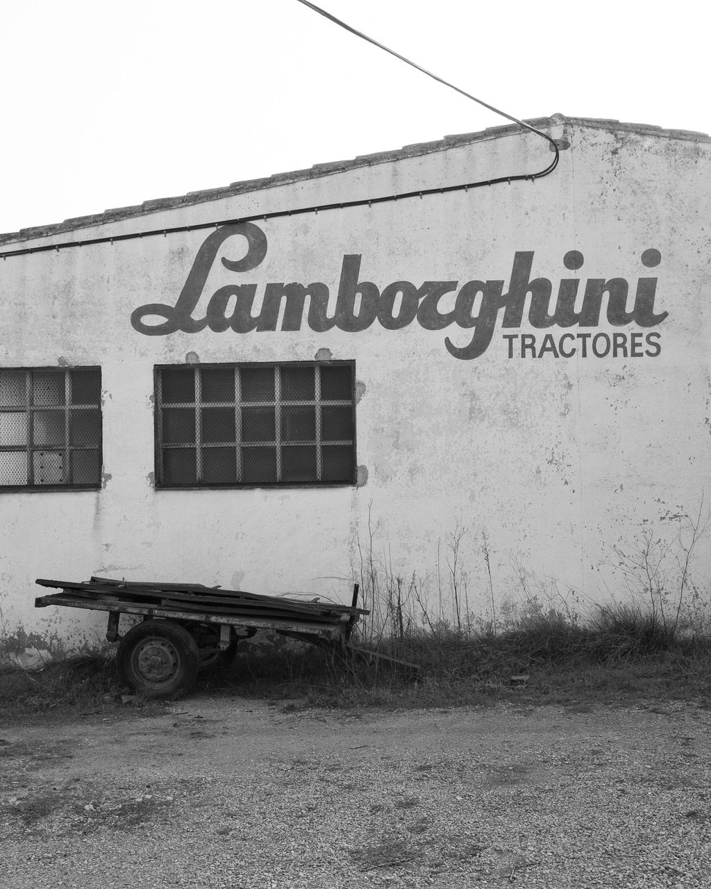 La fachada abandonada de un taller de Lamborghini Tractores en Castellón, con rótulo original visible y un remolque en desuso apoyado contra el muro agrietado.