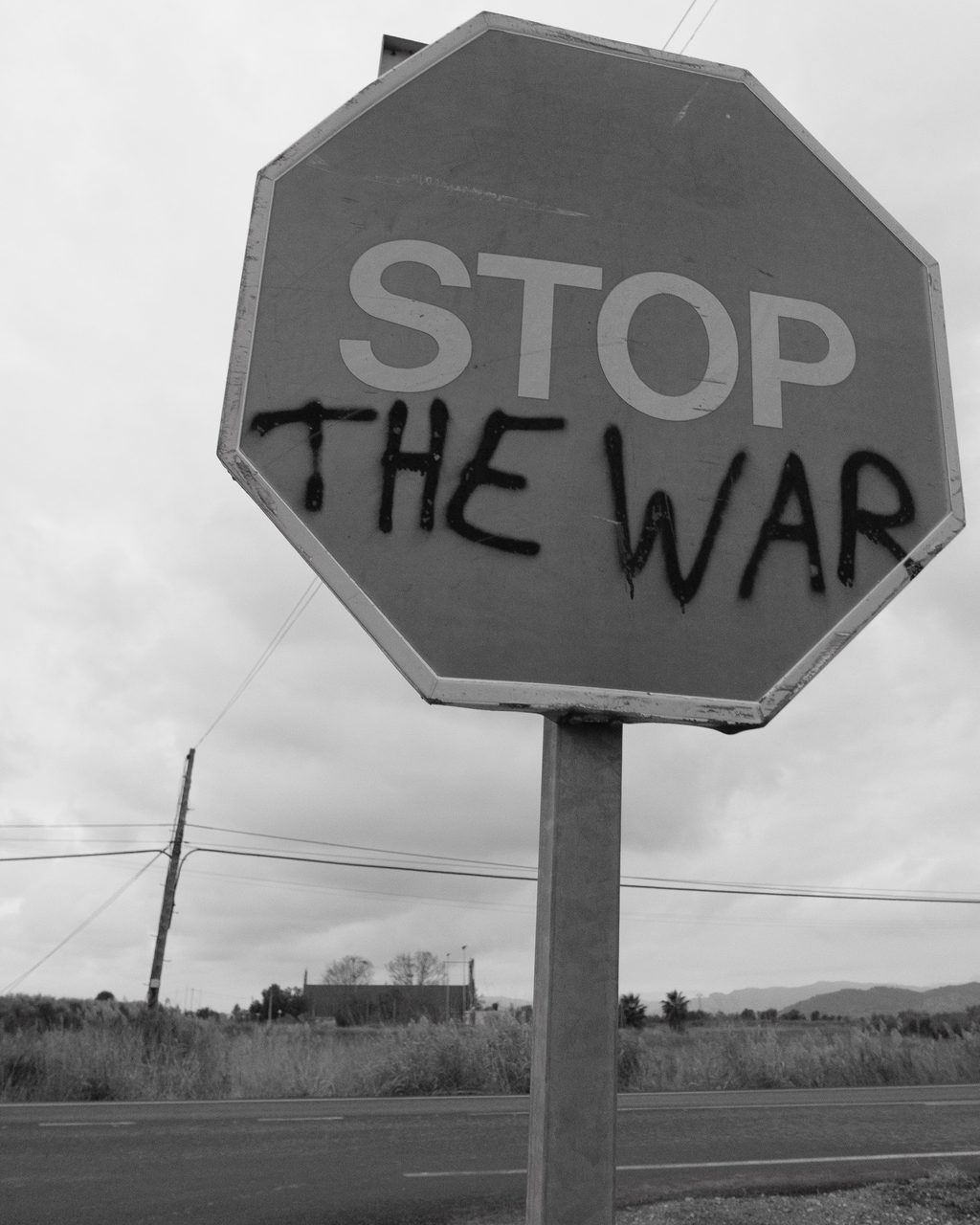Una señal de STOP intervenida con la frase “THE WAR” en aerosol negro en una carretera rural de Valencia, formando el mensaje pacifista “STOP THE WAR”.
