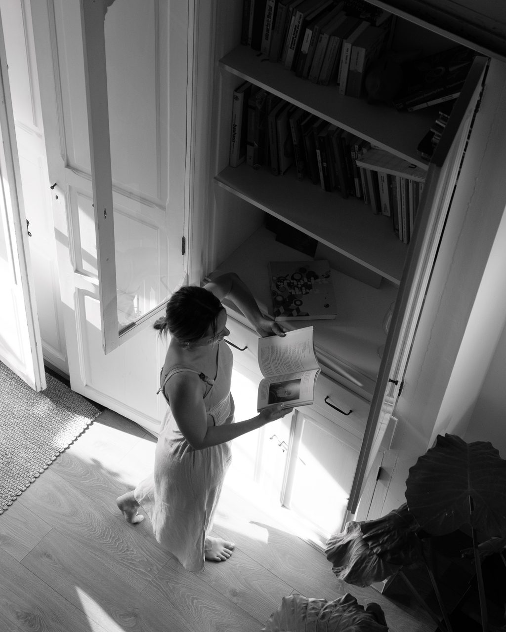 Una mujer descalza leyendo un libro en el interior de una antigua casa de pescadores del Cabanyal, Valencia, con luz natural entrando por las puertas de madera.