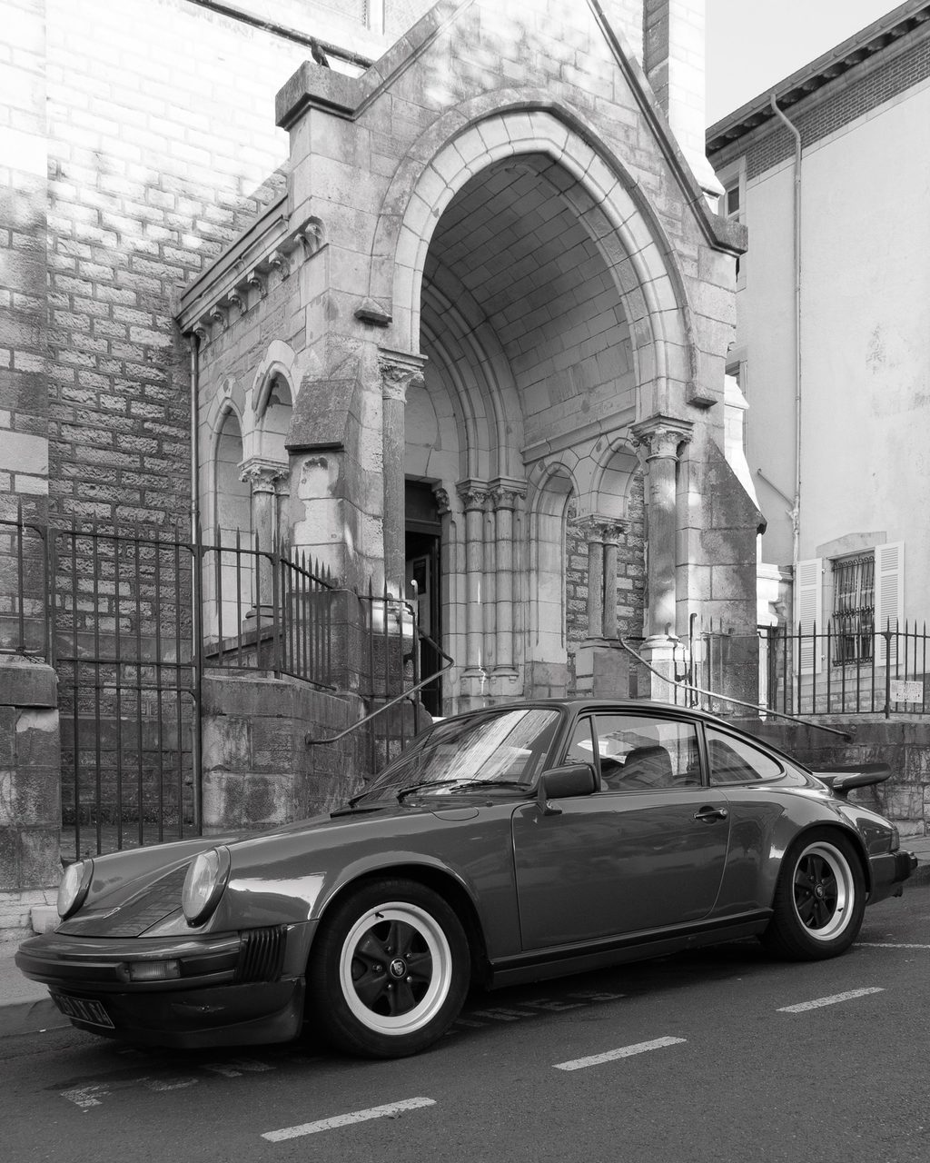 Un Porsche clásico aparcado frente a una iglesia de piedra con arcos históricos en una calle de Biarritz, Francia.