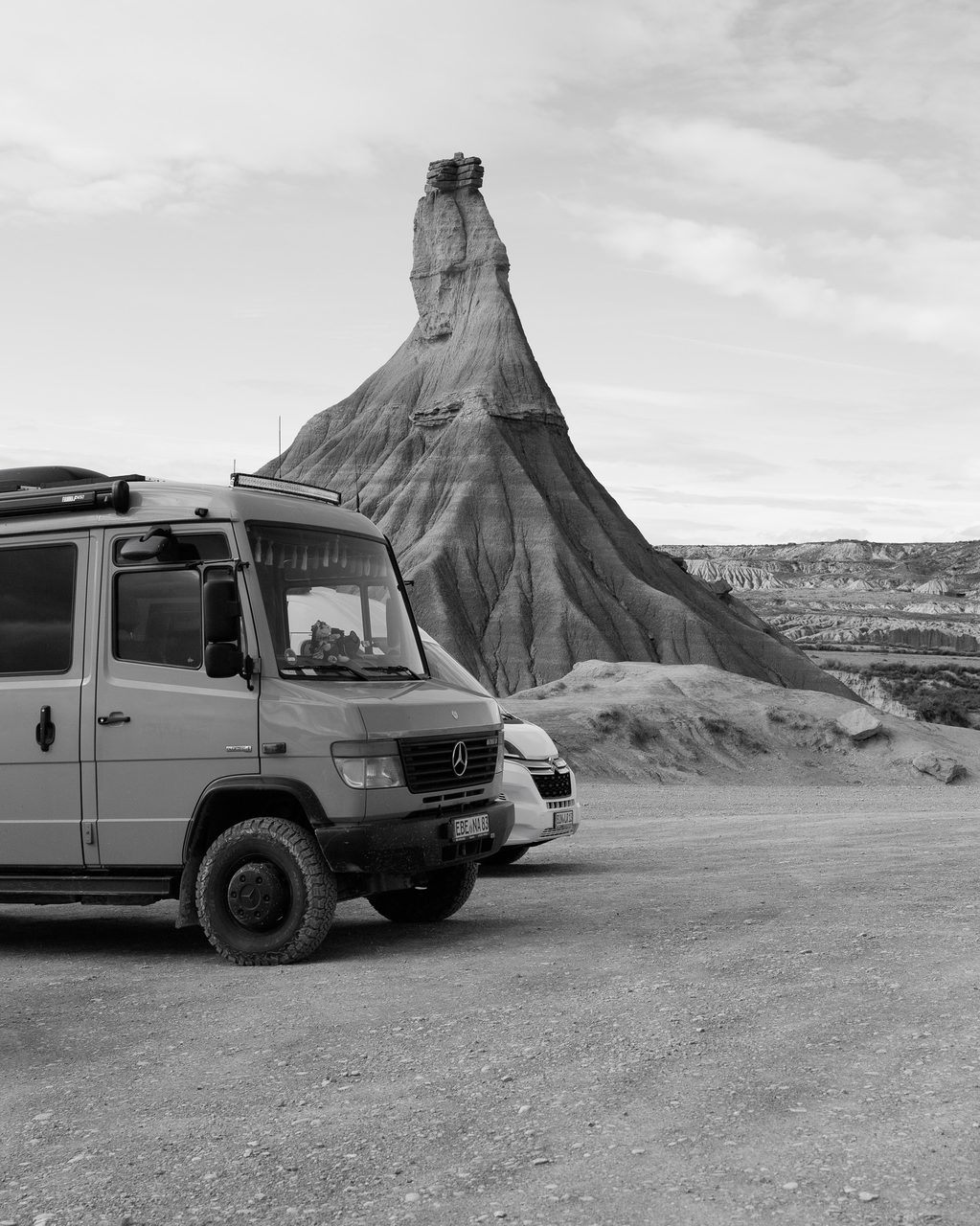 La formación rocosa Castildetierra en las Bardenas Reales de Navarra, con furgonetas de viajeros estacionadas en primer plano y un cielo azul con nubes.