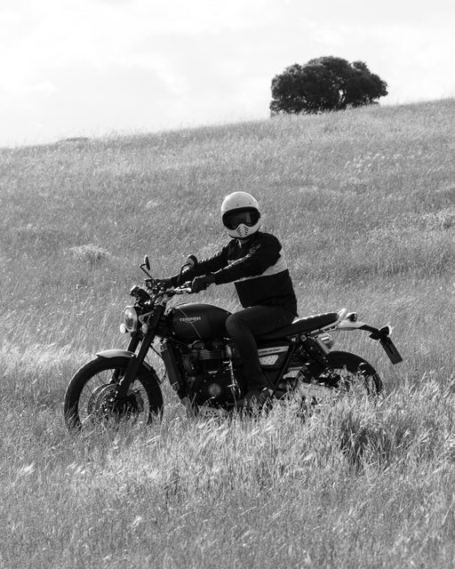 Motorista con casco sobre una Triumph cruzando un campo de hierba alta cerca de Madrid