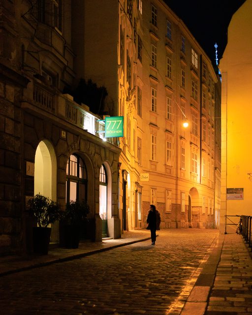 Calle histórica de Viena iluminada por farolas doradas con un caminante solitario