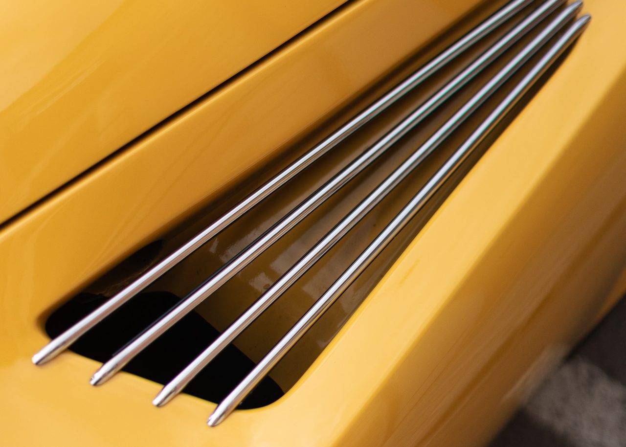 Detalle de las lamas metálicas de ventilación y la carrocería amarilla curvada de un Alpine A110 clásico en Madrid.