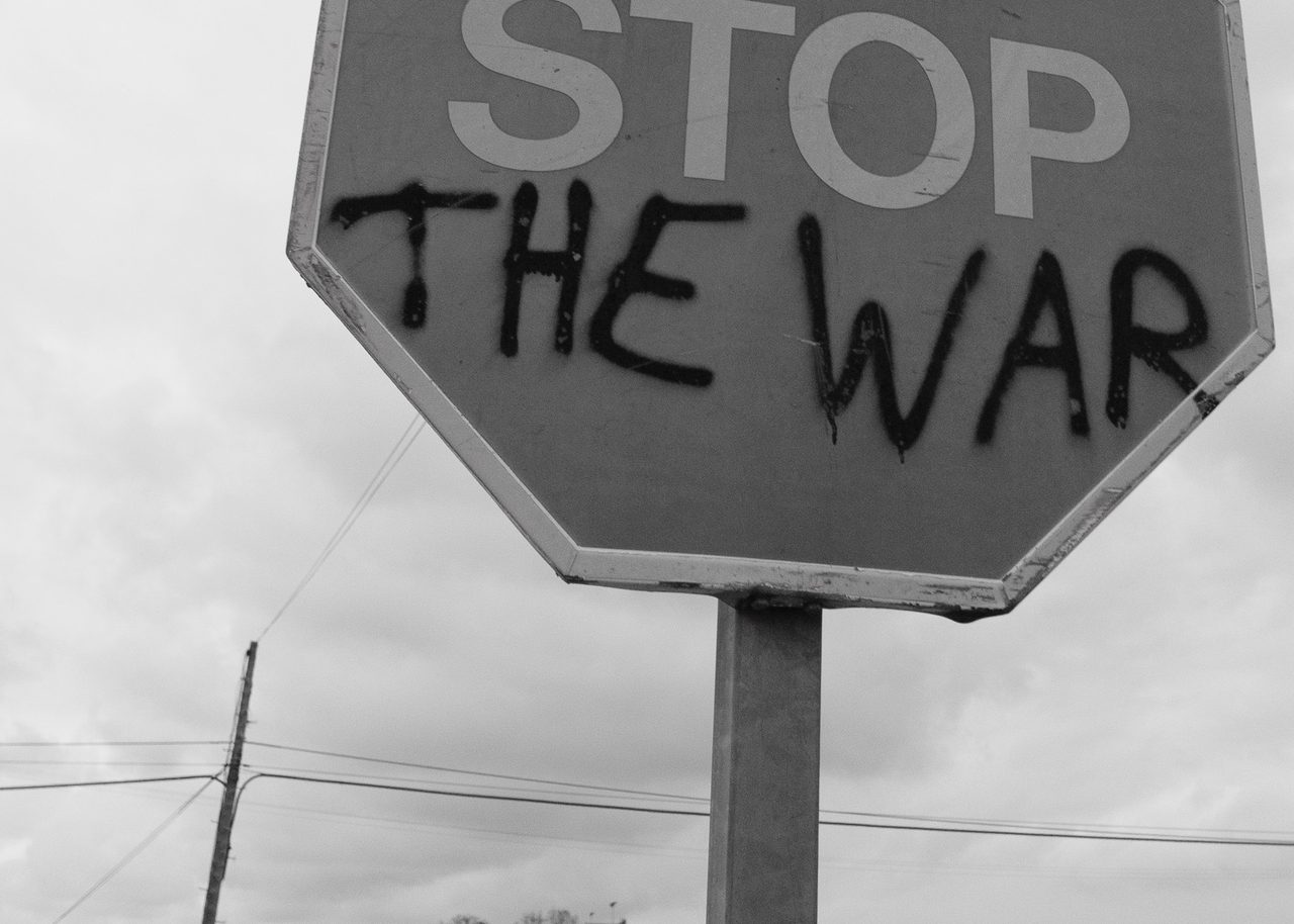 Una señal de STOP intervenida con la frase “THE WAR” en aerosol negro en una carretera rural de Valencia, formando el mensaje pacifista “STOP THE WAR”.