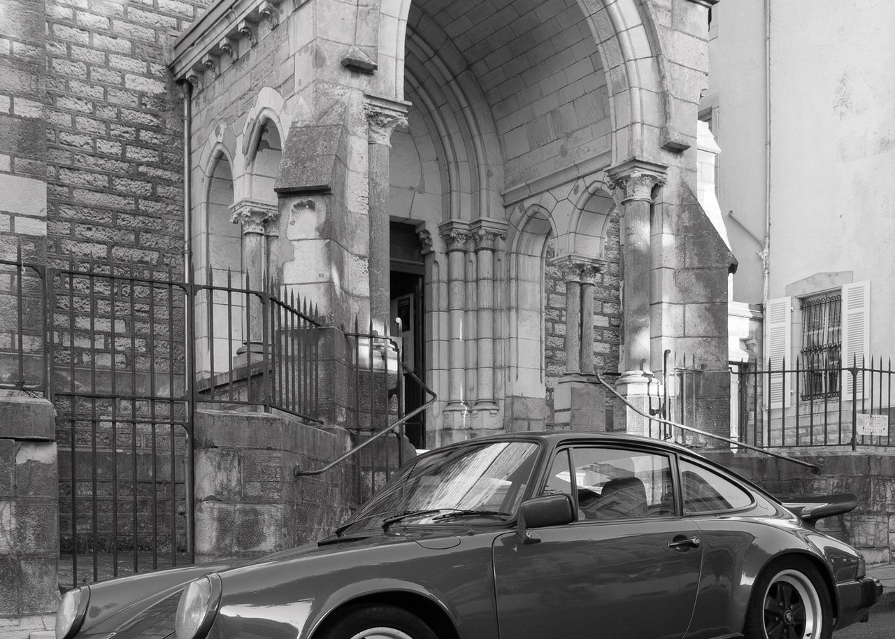 Un Porsche clásico aparcado frente a una iglesia de piedra con arcos históricos en una calle de Biarritz, Francia.