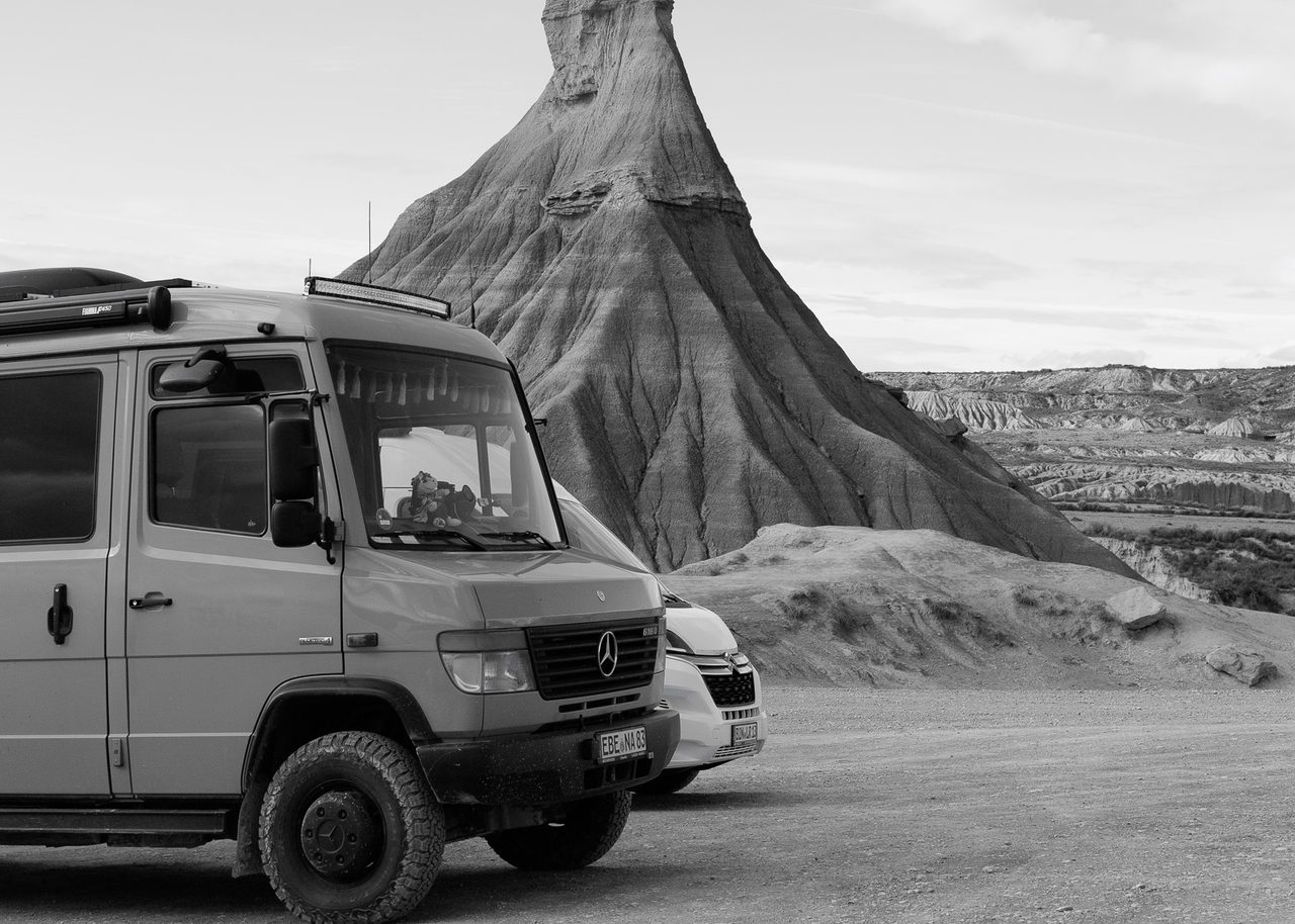 La formación rocosa Castildetierra en las Bardenas Reales de Navarra, con furgonetas de viajeros estacionadas en primer plano y un cielo azul con nubes.