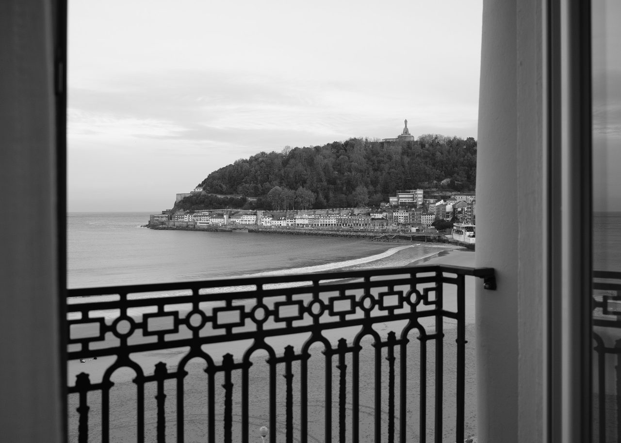 Amanecer en San Sebastián en blanco y negro enmarcado por el balcón de hierro forjado del Hotel de Londres y de Inglaterra, con la bahía de La Concha y el monte Urgull al fondo.