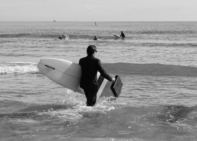 Participante disfrazado de ejecutivo entrando al mar con tabla de surf en el Festival Quasimoto