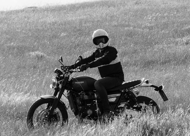 Motorista con casco sobre una Triumph cruzando un campo de hierba alta cerca de Madrid