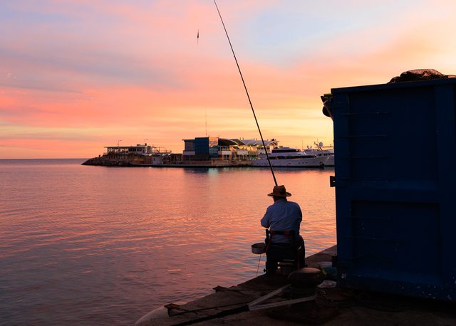 Hombre pescando al atardecer en el muelle del puerto de Burriana, Castellón
