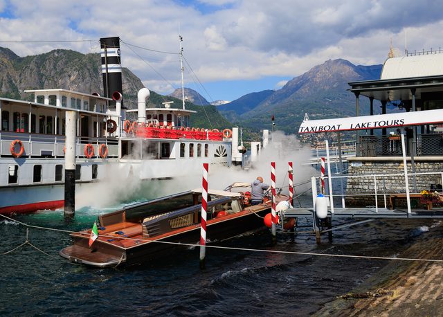 Barco de vapor y taxi boat de madera con bandera italiana en el muelle de Bellagio