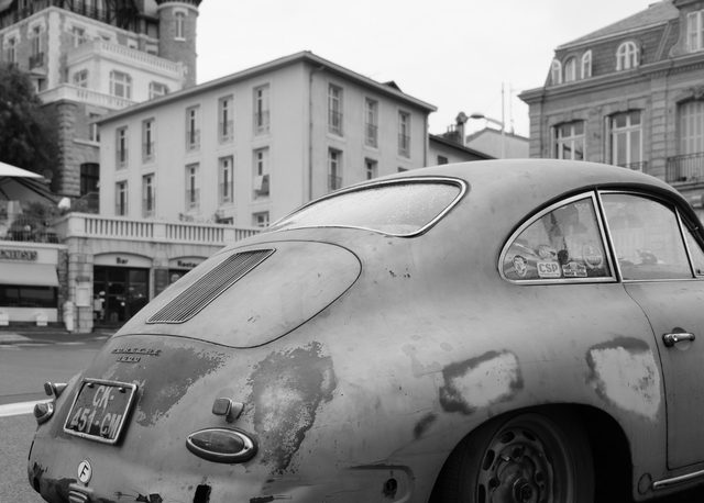 Porsche 356 envejecido en una calle de Biarritz con arquitectura clásica y pavimento húmedo