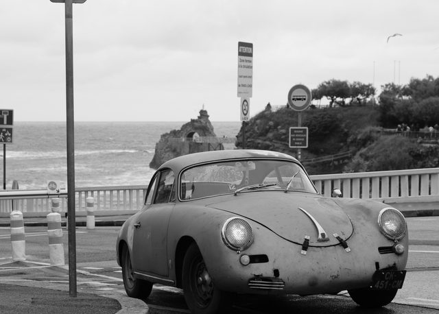 Porsche 356 envejecido junto a los acantilados de Biarritz con gaviota en vuelo