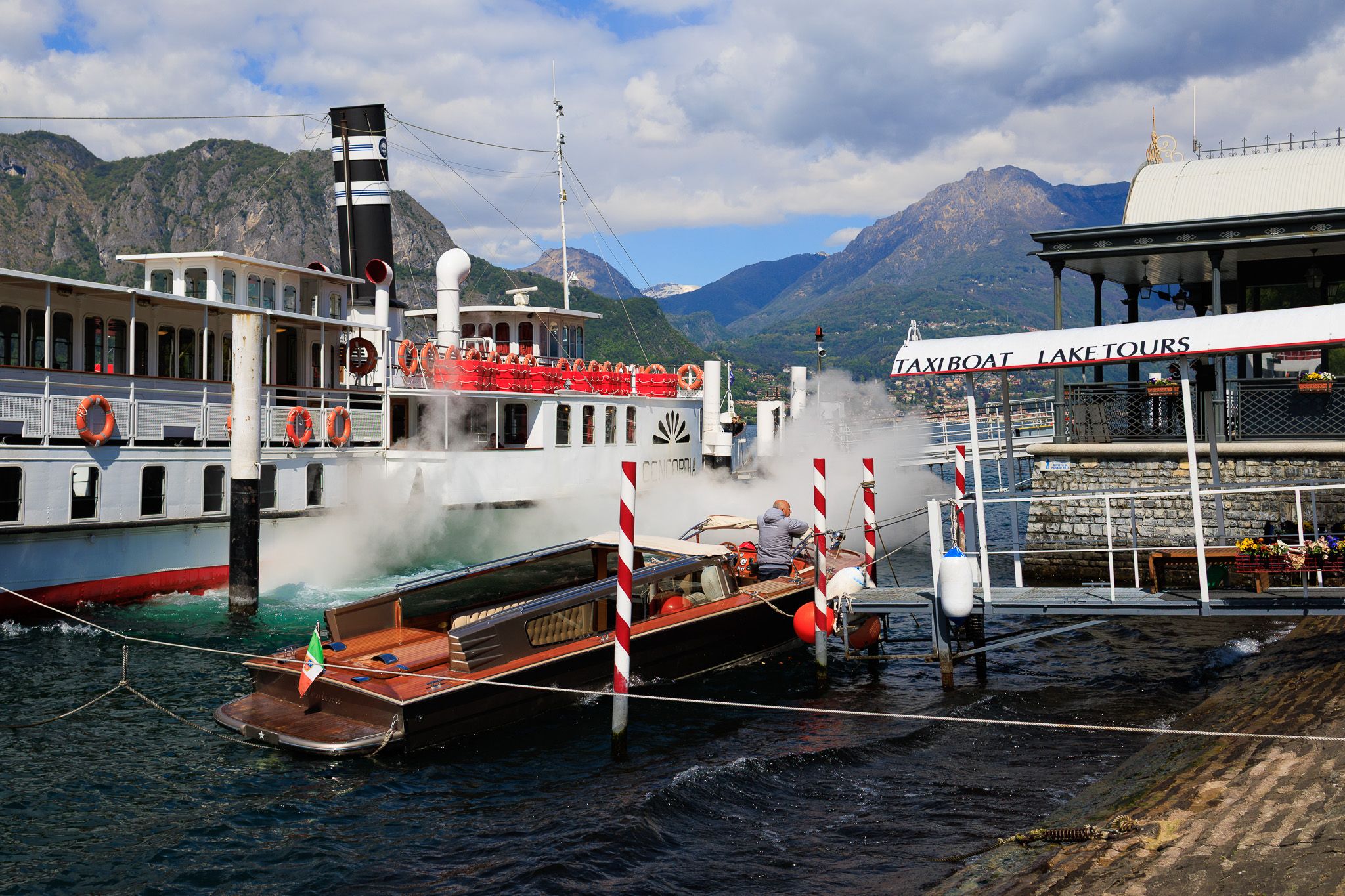 Barco de vapor y taxi boat de madera con bandera italiana en el muelle de Bellagio